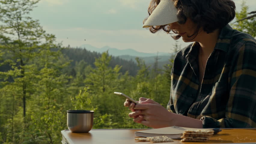 Traveler, woman traveler is deeply involved Smartphone in the hands of a girl who travels in the mountains under the open sky. active woman explores highlands uses modern technology while traveling
