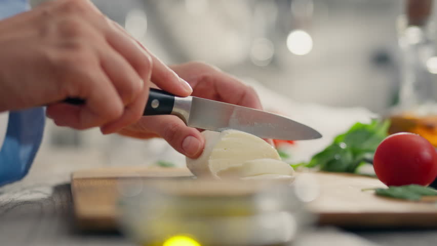 Basil leaf, white race girl slicing mozzarella intently on the kitchen table. a young parent cuts a piece of cheese with a knife uses various ingredients of vegetables and cheese, tomatoes Royalty-Free Stock Footage #1107582805