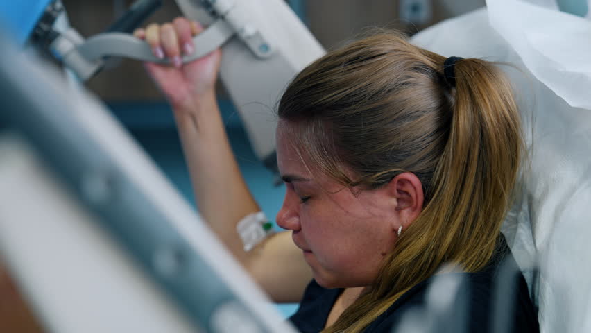Painful process of childbirth. Caucasian woman becomes red as she pushes a baby. Side view portrait.