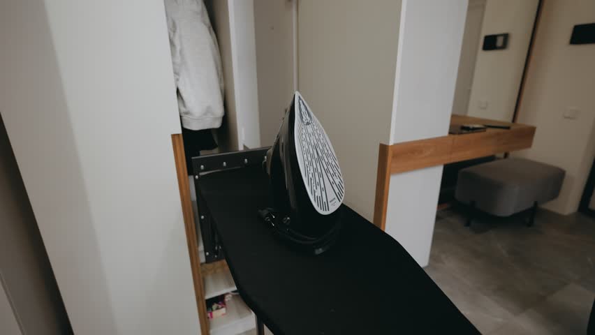 iron for ironing clothes. In a nice apartment in the corridor, there is an iron on a black ironing board, which is supposed to iron clothes. A housewife is ironing a shirt. Clothes for going out. Clea
