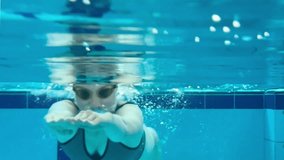 Girl or woman swims underwater in the pool. Shooting a video underwater as a woman swims in a pool. View of a woman swimming in a pool. Slowmotion pool video.
