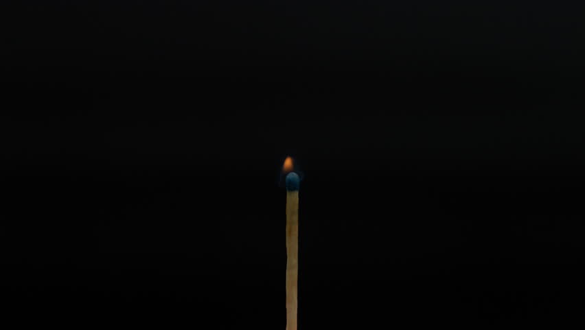 A match is ignited by a flame. The head is burning very fast until the wooden stick is on fire. The matchstick is on a dark background in a studio environment.