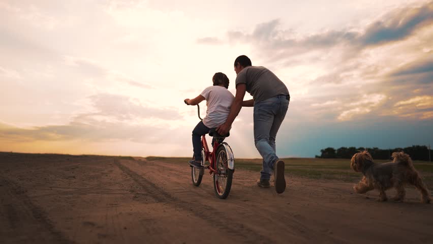 Father's Day. A father teaches his daughter to ride a bike. Daughter child learn to ride a bike at sunset in the park. Happy family on a bike in a summer meadow. Active game with a bike on a picnic Royalty-Free Stock Footage #1107603135