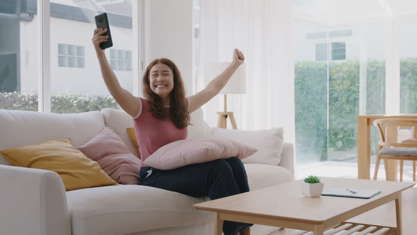 Asia people adult woman looking at mobile phone joy win luck bet online game at home sofa. Young attractive Gen Z girl got lucky loan making money sale reward on shopping discount promotion benefit.