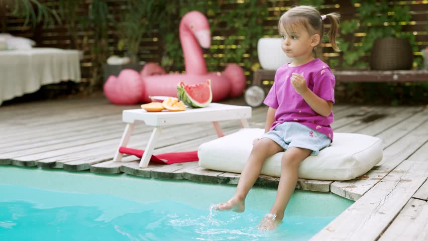 Funny cute girl on summer vacation. Child has fun on the beach. Cute baby girl in a colorful swimsuit and sunglasses is resting and eating fruit. 