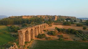 In this breathtaking aerial stock video, the mesmerizing ruins of an aqueduct stand gracefully near the ancient city of Aspendos in the captivating region of Antalya, Turkey. The camera sweeps above