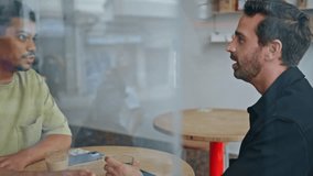 Couple male friends meeting in cozy cafe view through window close up. Two multiethnic guys talking laughing together at friendly gathering. Cheerful men speaking joking sharing news in coffee house. - Powered by Shutterstock - Get 15% off with code: PIKWIZARD15