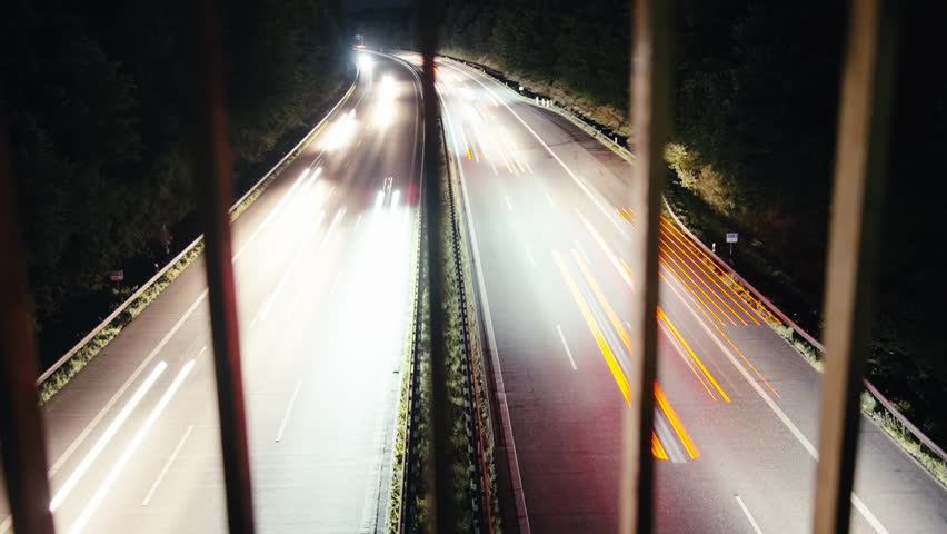 Time lapse of busy motorway at night. Filmed from high angle with a wide angle lens and slow shutter speed. Light trails of fast cars rushing by. High contrast. 4K footage.