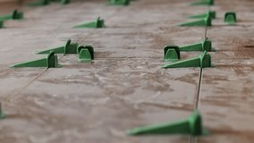 Tile levelling system, four plastic green clips with wedges. Close-up view, selective focus, blurred background.
