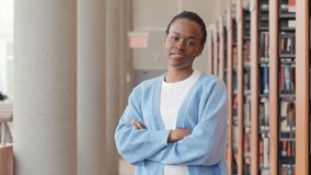 Happy cute African teenage girl, smiling confident short-haired cute Black ethnic college student standing arms crossed looking at camera in modern foreign university campus library. Portrait.