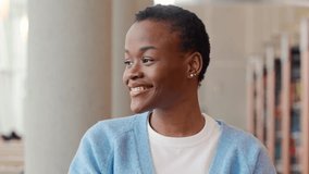 Happy cute African teenage girl, smiling confident short-haired cute Black ethnic college student standing looking at camera in foreign university campus library. Close up face portrait.