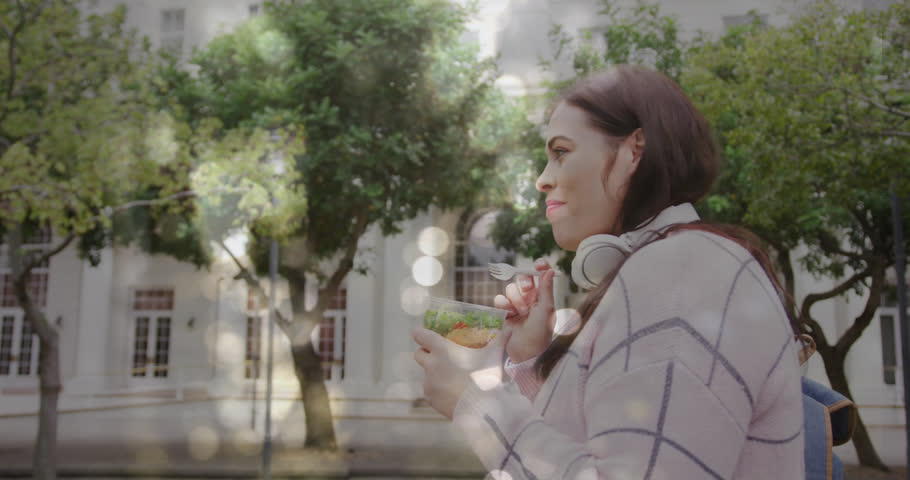 Animation of spots of light over caucasian woman eating take away lunch in city street. Lifestyle, urban living and happiness concept digitally generated video.