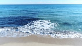 Shore of a beach while the small waves of the sea arrive creating white foam on the sand, on a clear day and the horizon in the background as a straight line that separates the sea from the sky.4k