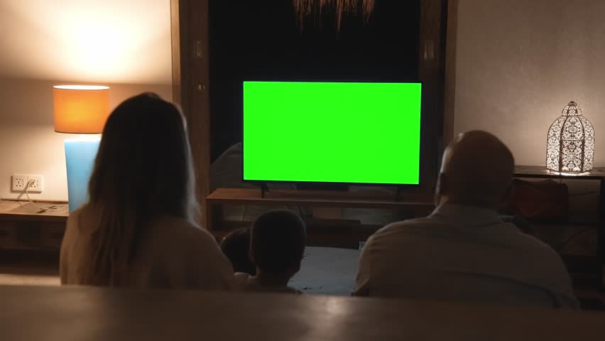 Happy Family of Parents with Young Kids Watching TV and Sitting on Sofa. People Inside at Home Watch News on Television Display Mockup. Children on Couch Looking at White Screen of Chroma Key Mock Up Royalty-Free Stock Footage #1107629683