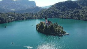 Church of the Assumption of Mary in the center of the lake Bled. Slovenia. Aerial. Summer. Drone video. Flying around small island on Bled Lake. Blue water and forest around.