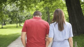 A middle-aged Caucasian couple walks down a pathway through a park on a sunny day - view from behind - Powered by Shutterstock - Get 15% off with code: PIKWIZARD15