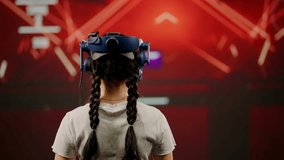 The little girl use tracking controllers in her hands, moves actively immersing herself in modern game. The child wearing VR headset plays game. Behind girl there is screen with blur background image - Powered by Shutterstock - Get 15% off with code: PIKWIZARD15