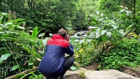 Photographer taking pictures of a river in the middle of the nature surrounded of green trees and moss
