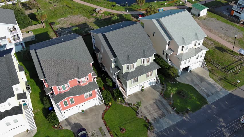 tilt aerial footage of Carolina Lake with homes, lush green trees and grass, boats, docks and cars driving on the street with a gorgeous clear blue sky in Carolina Beach North Carolina USA