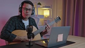 Asian man youtuber live streaming perfomance playing guitar and sing a song. Asian man teaching guitar and singing online. Musician recording music with laptop and playing acoustic guitar. - Powered by Shutterstock - Get 15% off with code: PIKWIZARD15