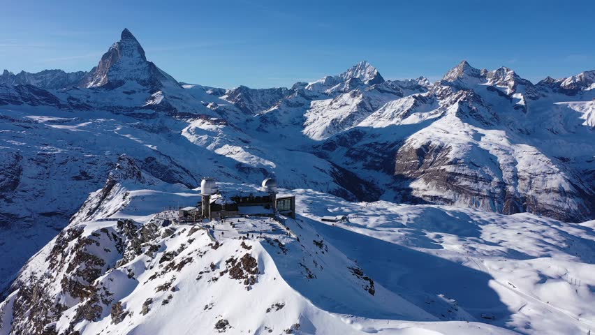Scenic aerial view of mountain ridge Gornergrat in Pennine Alps covered with snow with building of hotel, observatory and rack railway station on background of Matterhorn peak, Zermatt, Switzerland