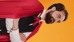 Vertical video Powerful fantasy hero with red cape standing against yellow background, feeling determined and confident on camera. Dedicated butler acting like superhero, staff member having mantle.