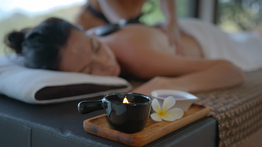 Close up of aroma lamp at the massage table with girl lying on it, back massage with stones and hands, relaxation in health spa resort, body care concept Royalty-Free Stock Footage #1107673441