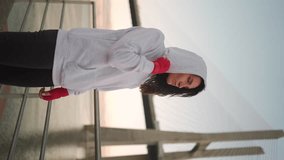 Athletic middle age female boxer dressed hoodie warming up arm and leg muscles before training. Kickboxer woman prepares for boxing workout outdoor on pier. Vertical video