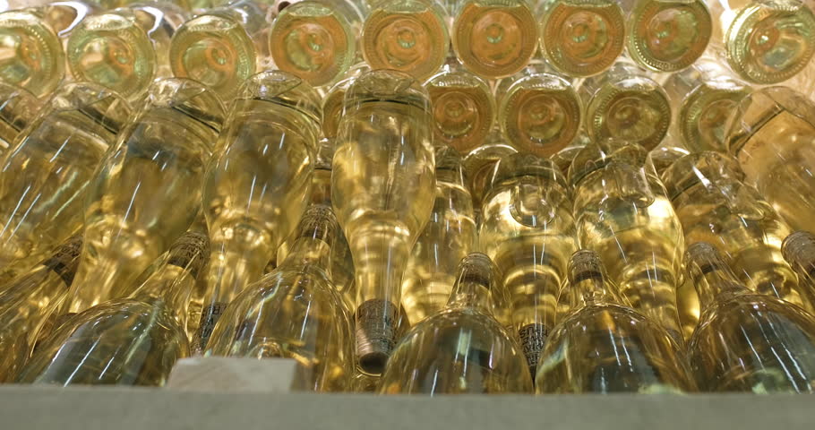 Factory worker stacking wine bottles with white wine in container. Wine production factory