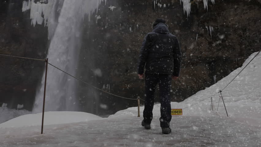 Back View of Man in Snowfall Walking Under Waterfall on Cold Winter Day and Raising Arms, Slow Motion