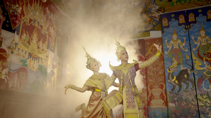 Beautiful Asian woman wear Thai traditional dress action of dancing together with man stand in front of Thai painting on public place wall. Royalty-Free Stock Footage #1107680089