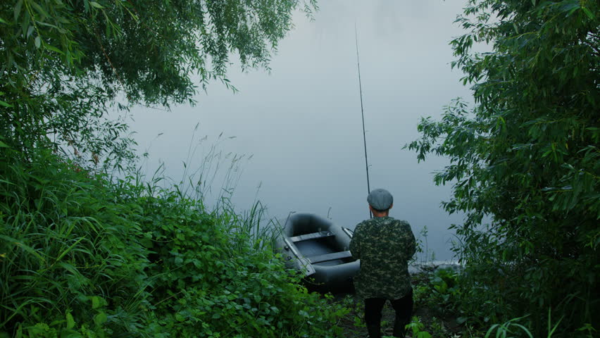 A man on the shore of the lake prepares a fishing rod before fishing on a boat