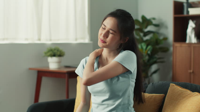 Tired beautiful young asian woman sit on couch rubbing neck to relieve muscle tension. Attractive female suffer from pain massaging shoulder stress relief from overwork sit on sofa at cozy living room Royalty-Free Stock Footage #1107684111