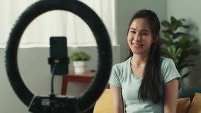 Beautiful young asian woman using mobile phone recording, live streaming a video vlog sharing on social media. Asian female blogger online live streaming, video call sitting on sofa at home.