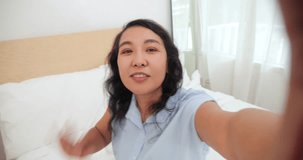 Happy women in prosthetic leg waving hands while video call, sitting on bed at home. Asian women amputee showing prosthetic leg while making, greeting video call. Leg prosthetic equipment