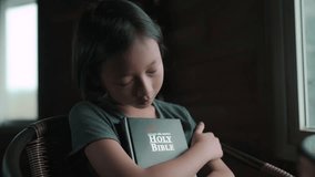 Child girl hugging the bible and sleeping in chair, christian concept. High quality 4k video.