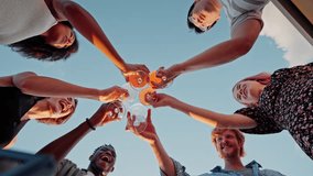 Bottom view of six multiracial colleagues clinking glasses with alcohol drinks during corporate party on open air. Happy people in classy outfits celebrating successful business deals. - Powered by Shutterstock - Get 15% off with code: PIKWIZARD15