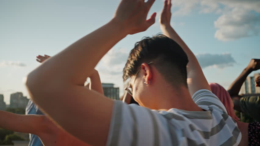 Close up of diverse stylish friends dancing rhythmically on rooftop terrace while hanging out together during summer party. Concept of youth, leisure time and relaxation. Royalty-Free Stock Footage #1107689193