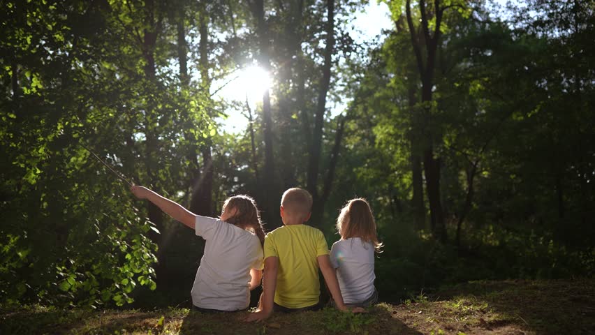 children sit on the banks of river. happy family childhood dream concept. a group of little children lifestyle sit together by the river and talk. kids spend time outdoors in nature in the forest