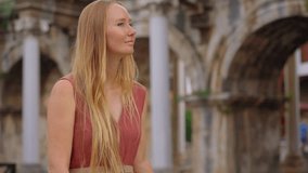 In this captivating video, a young woman tourist is portrayed visiting the renowned tourist attraction in Antalya - Hadrian's Gate. She stands before the majestic archway, adorned with intricate