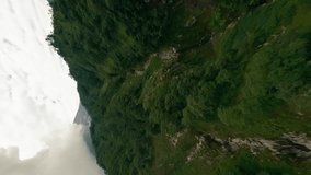 Vertical video. FPV drone slowly flying erupting volcano mountains ranges covered jungle forest plants frozen lava. Thick white smoke rises from volcano crater. Flying green nature landscapes disaster