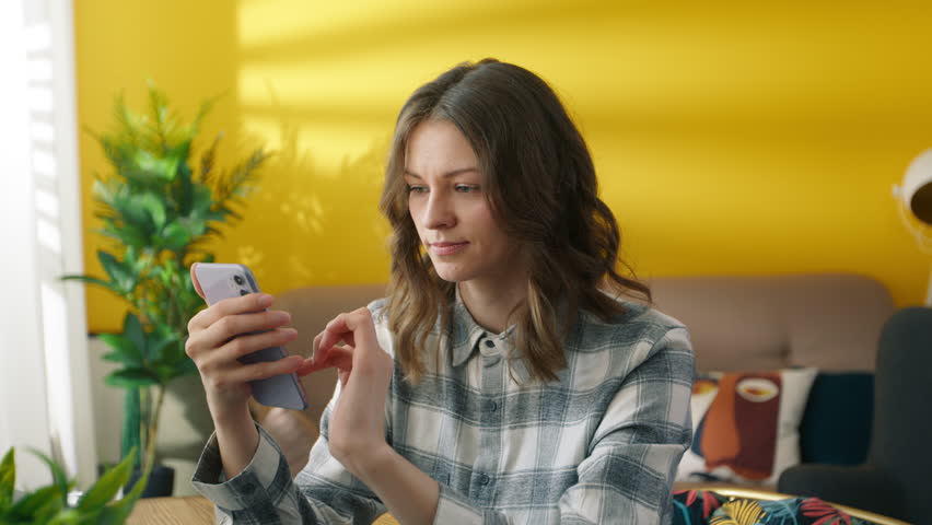 Focused woman scrolling internet pages on smartphone. Pretty girl browsing internet online. Collage student reading news on mobile phone. Young lady using cellphone at home. Youth concept, 4k footage