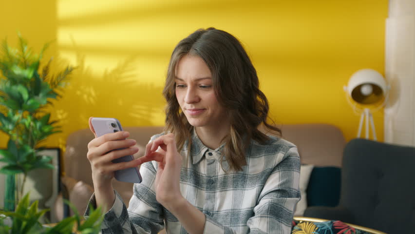 Focused woman scrolling internet pages on smartphone. Pretty girl browsing internet online. Collage student reading news on mobile phone. Young lady using cellphone at home. Youth concept, 4k footage