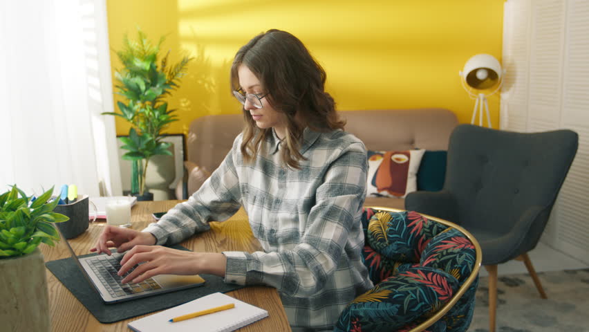 Confident woman working at remote workplace. Smart girl typing on laptop keyboard at home. Collage student learning online. Serious lady posing on camera. Female model holding hand on the chin