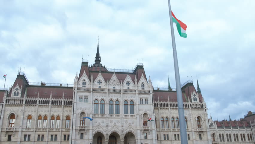 Hungarian flag by budapest parliament against sky. A view of waving Hungary flag against Budapest parliament in the day light.