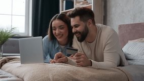 Caucasian happy couple woman and man relax on bed with laptop shopping online use bank credit card pay order buying in internet booking financial service e-commerce app winning success spending money - Powered by Shutterstock - Get 15% off with code: PIKWIZARD15