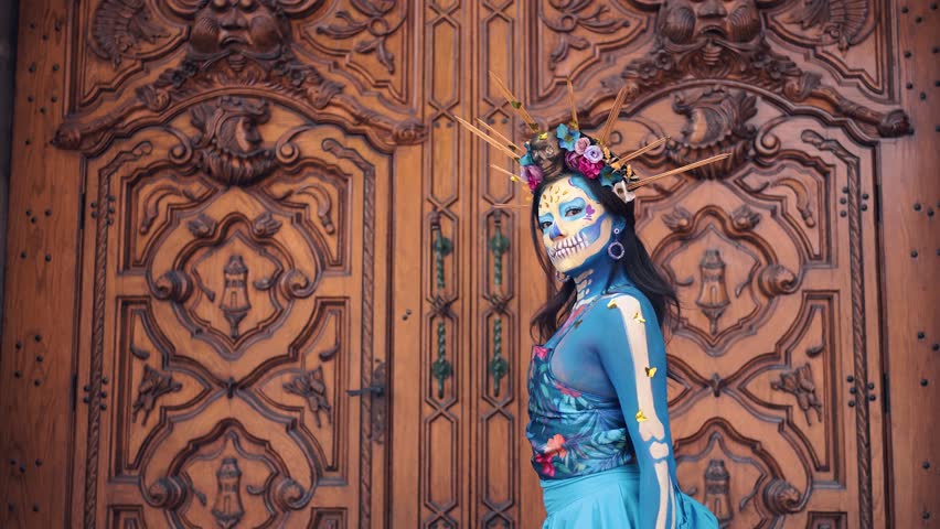 Dancer in costume for dia de los Muertos, woman with long dark hair in traditional costume and Mexico Catrina makeup standing near wooden ornamental door and holding skirt. Day of death Royalty-Free Stock Footage #1107696789