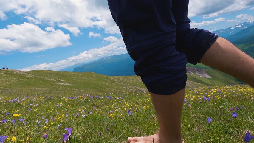 Man walking barefoot on grass and flowers in the mountains. Side view. Close up. Bare feet of a man with trousers rolled up to the knees walking on grass. The idea of freedom and happiness Royalty-Free Stock Footage #1107699125