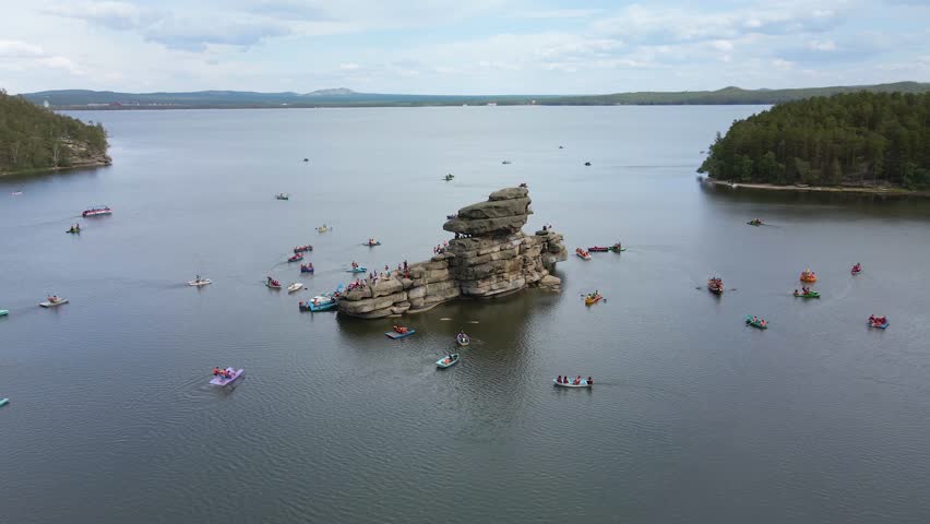 Boat trip on catamarans and boats.Stone island of Zhumbaktas in the middle of a mountain lake in Kazakhstan Borovoe.The rock in the middle of the water the Kazakh Sphinx.A lot of people on the water