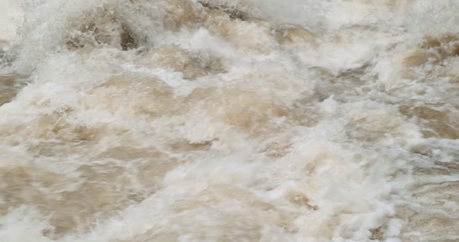 Brown fast mountain river water flowing, close up. Strong river flow in spring. Rapid muddy flood motion. Waterfall splashing. Dirty river with yellow water in flooding period during heavy rains. 4k
